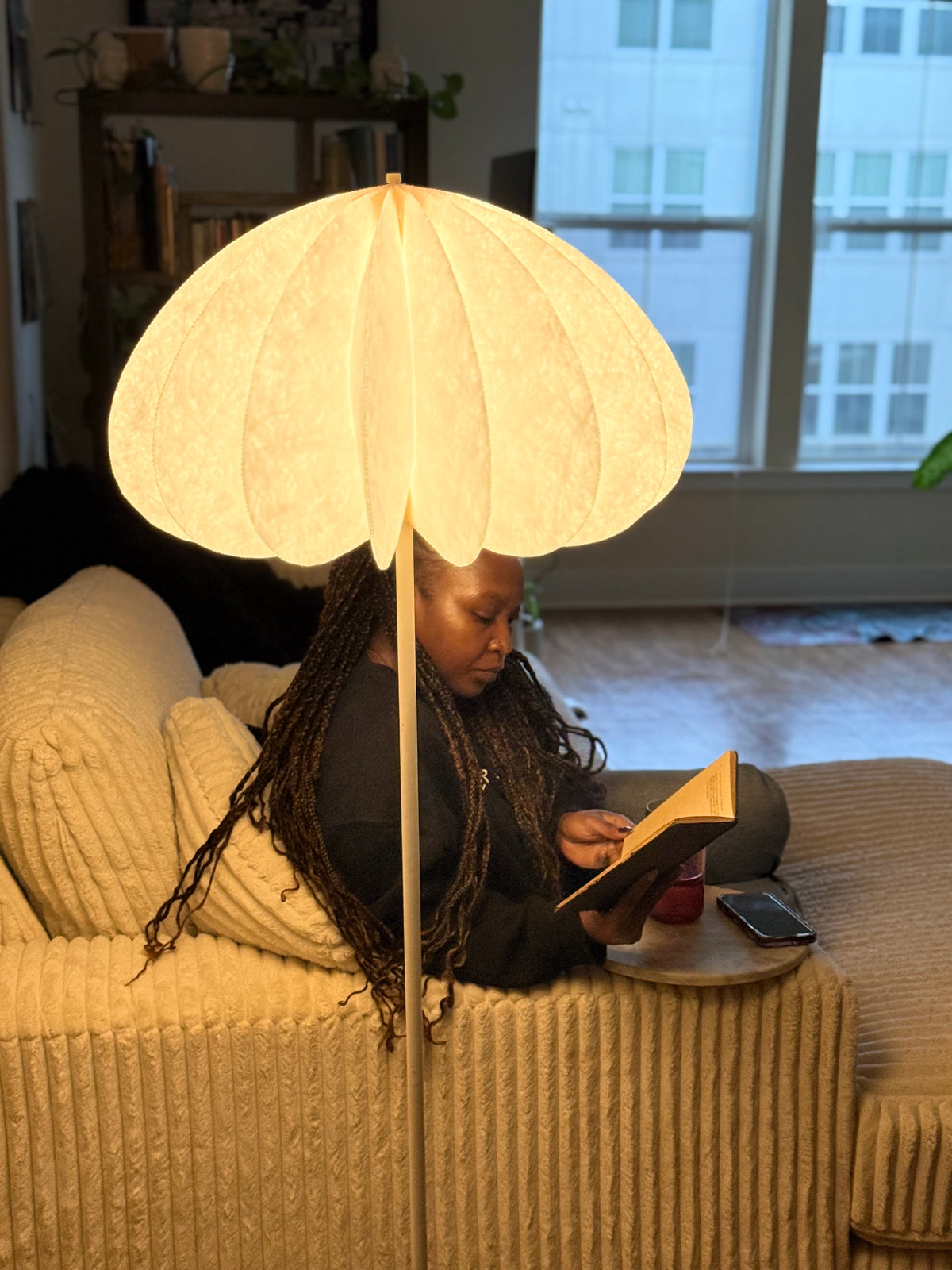 Dandelight floor lamp glowing over a person reading on a cream corduroy sofa